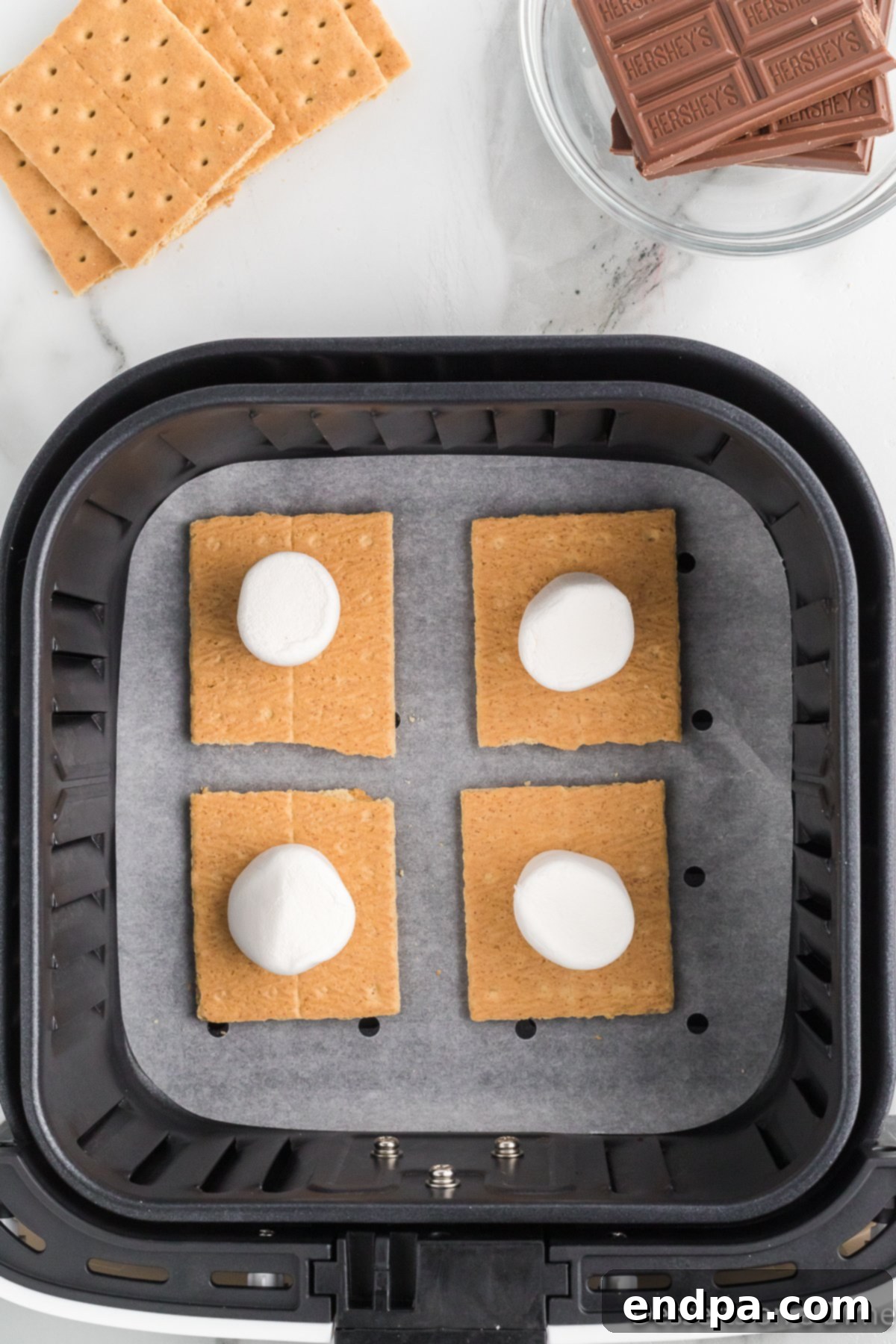 Marshmallows placed on graham cracker halves in an air fryer basket.