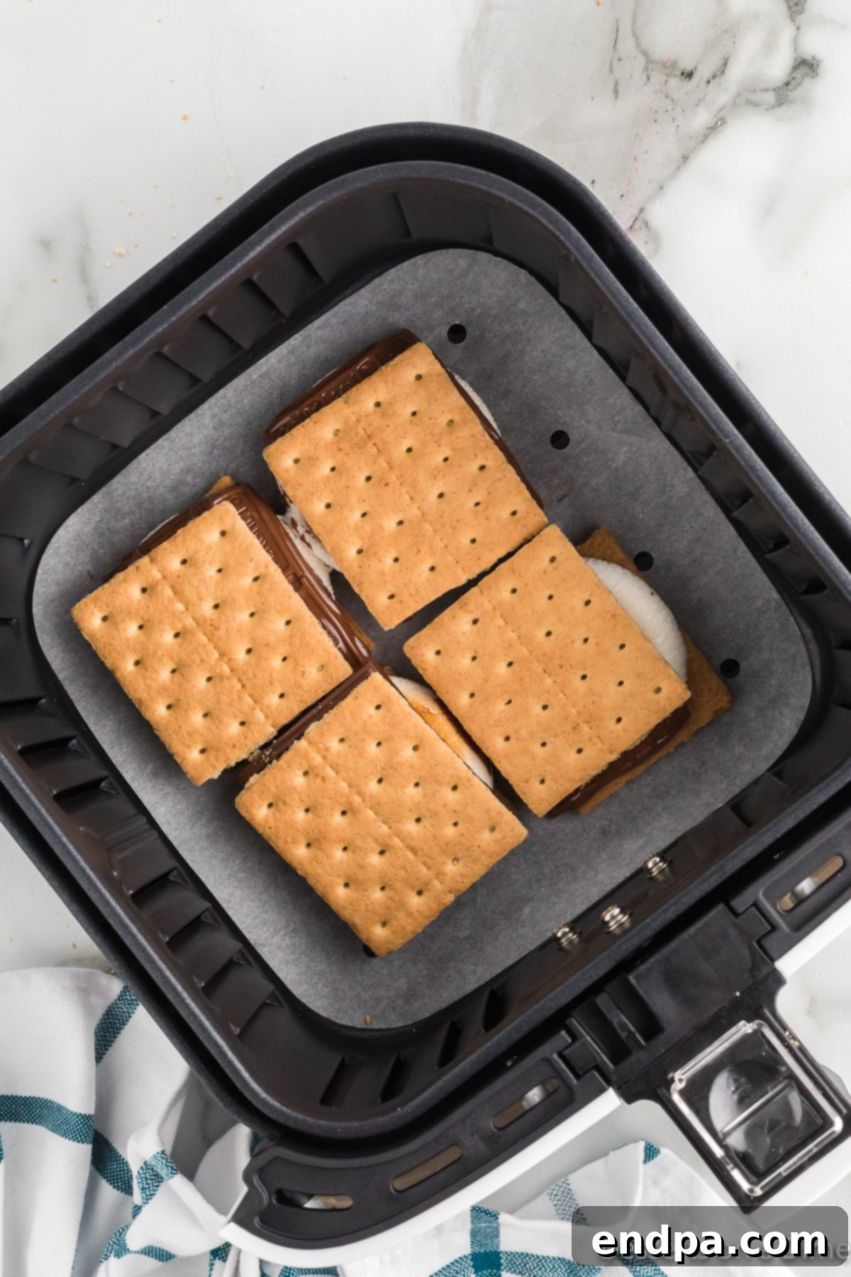 Melted chocolate added to toasted marshmallows, with top graham crackers being placed.