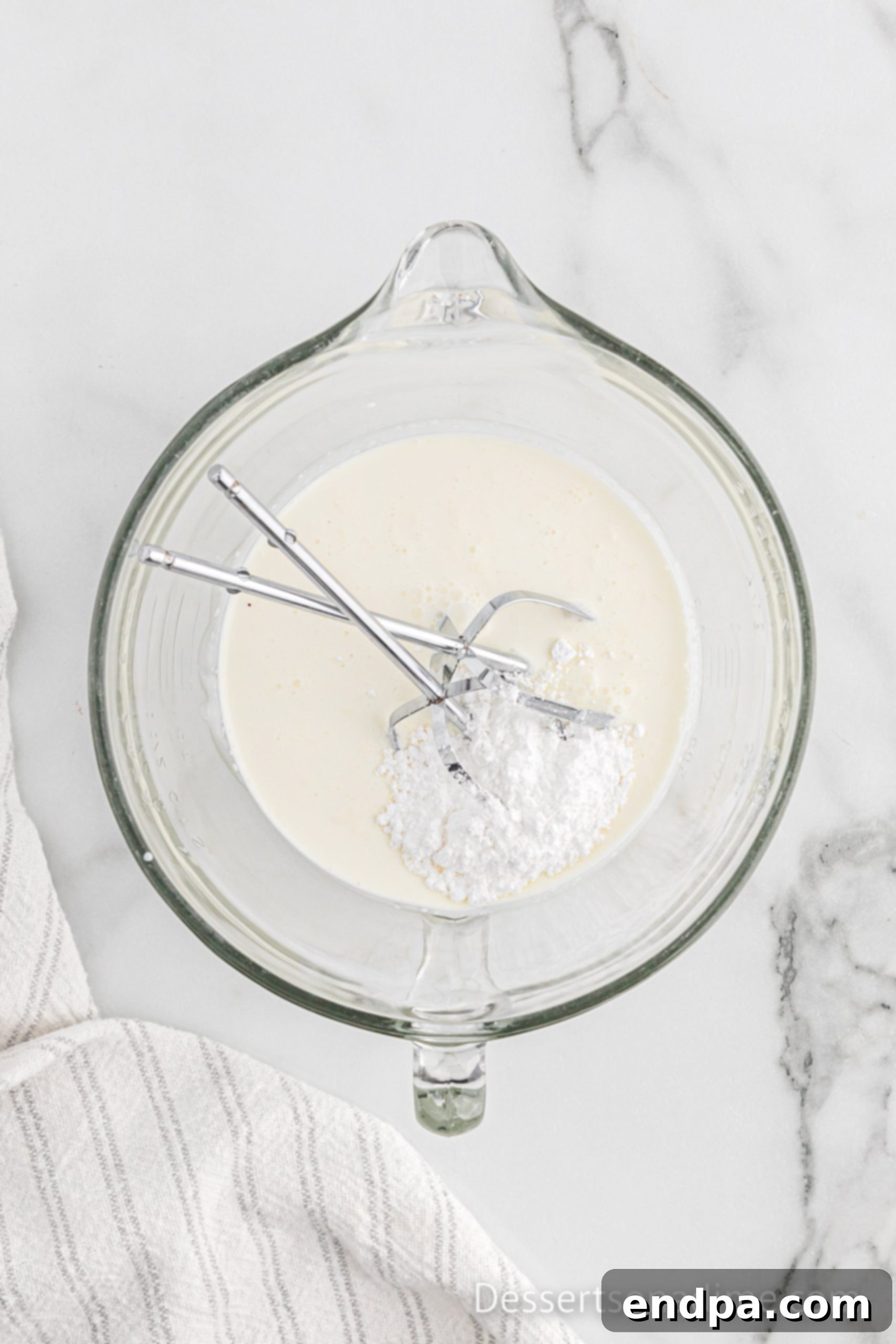 Heavy whipping cream and powdered sugar being whipped in a chilled bowl.