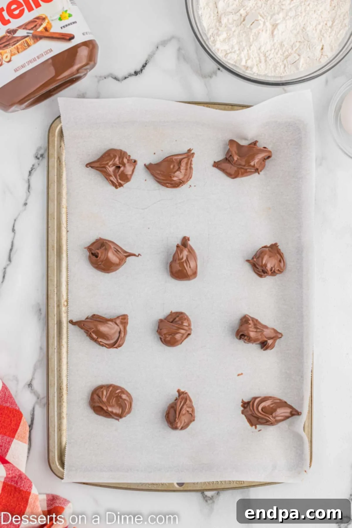 Dollops of Nutella carefully placed on parchment paper-lined baking sheets, ready for freezing.
