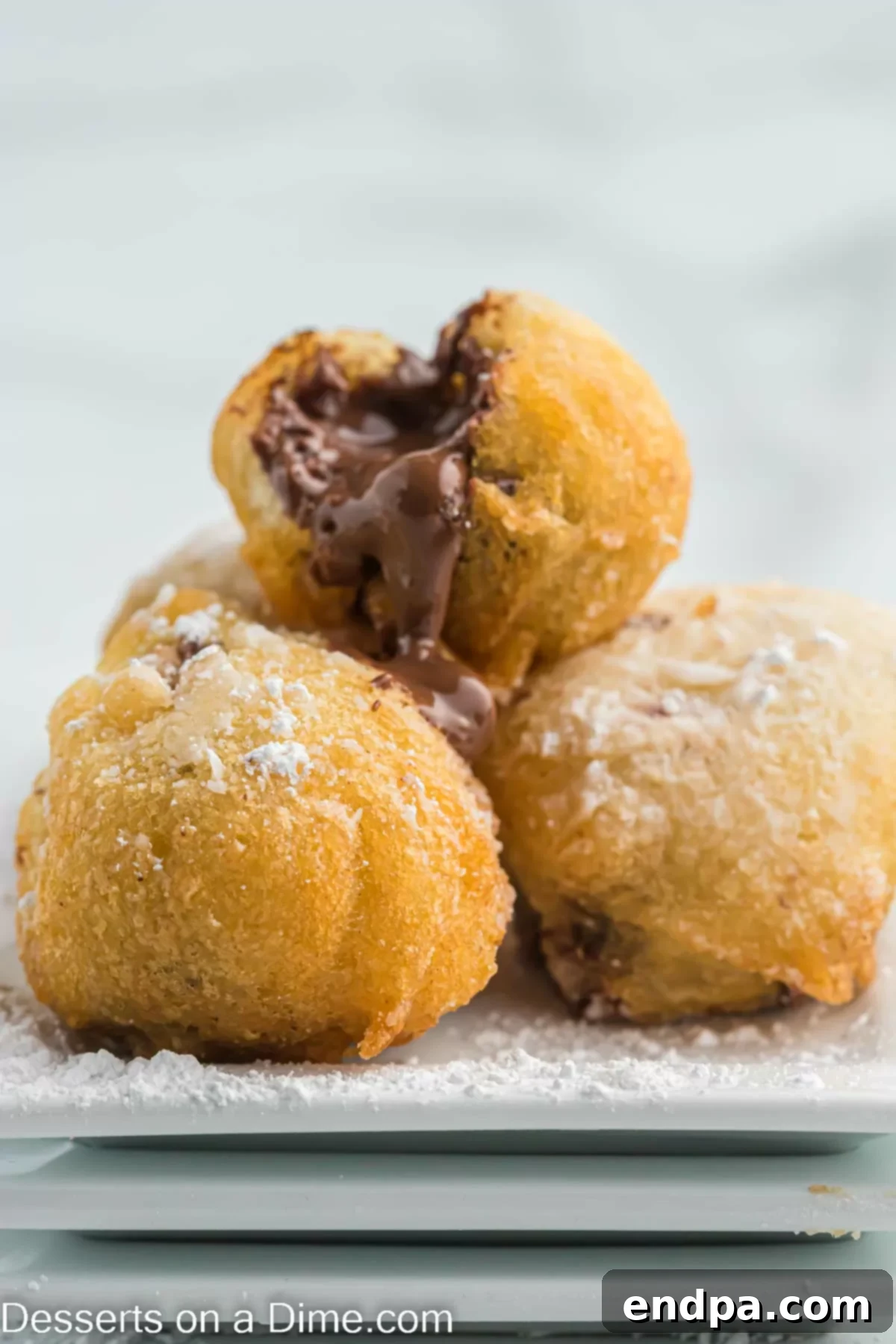 An appetizing stack of Deep Fried Nutella pastries, generously dusted with powdered sugar.