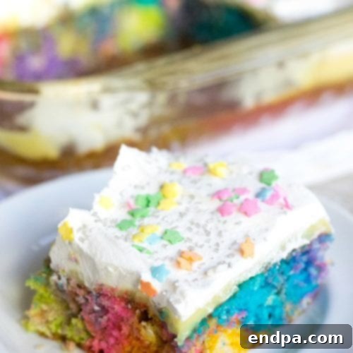 A vibrant, multi-colored Unicorn Poke Cake slice, decorated with sprinkles.