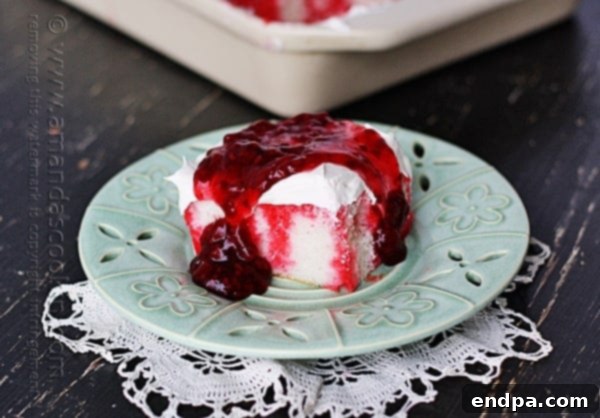 A luscious slice of Raspberry Dream Poke Cake, showing off its pink filling and raspberry topping.