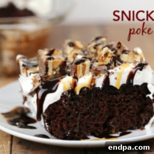A generous slice of Snickers Poke Cake, topped with chocolate, caramel, and chopped Snickers bars.