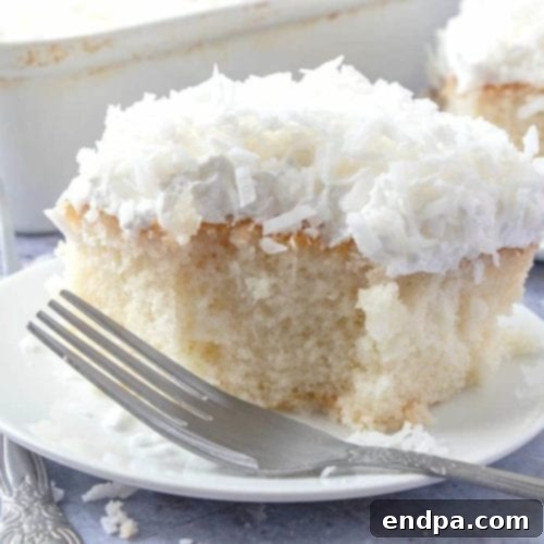 A slice of Coconut Cream Poke Cake, topped with shredded coconut.