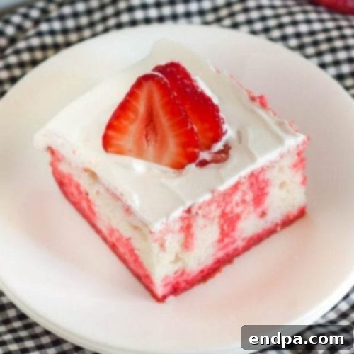 A vibrant slice of strawberry Jello poke cake topped with whipped cream and fresh strawberries.