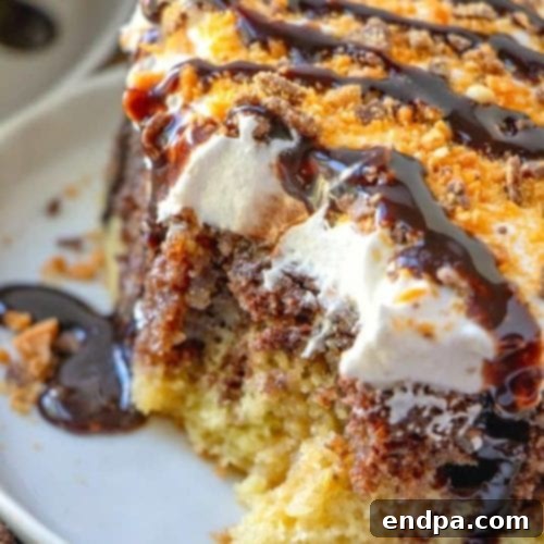 A slice of Butterfinger Poke Cake, showing off its caramel topping and crushed Butterfinger candy.