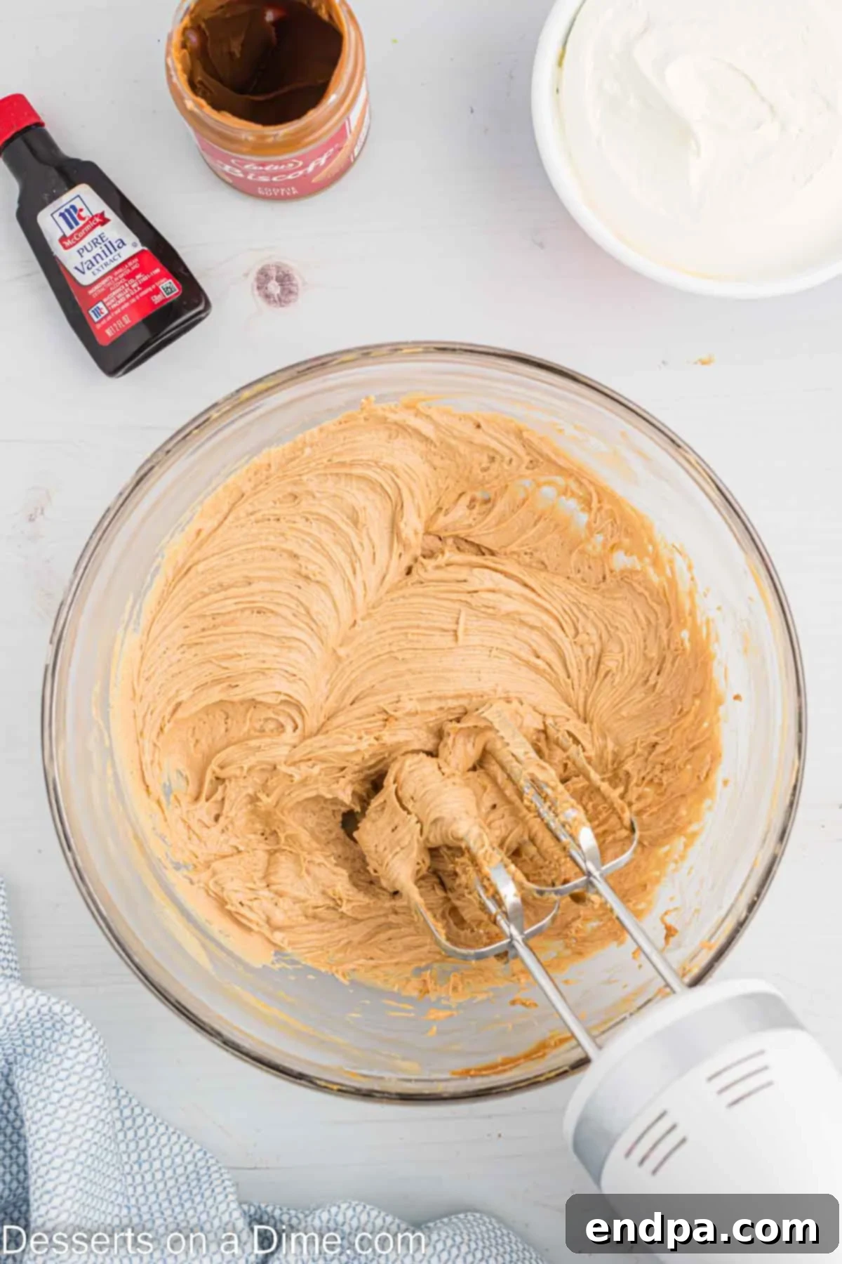Decadent Cookie Butter Cheesecake 6 Cream cheese, cookie butter, powdered sugar, and vanilla extract being combined in a large mixing bowl with a hand mixer until smooth.