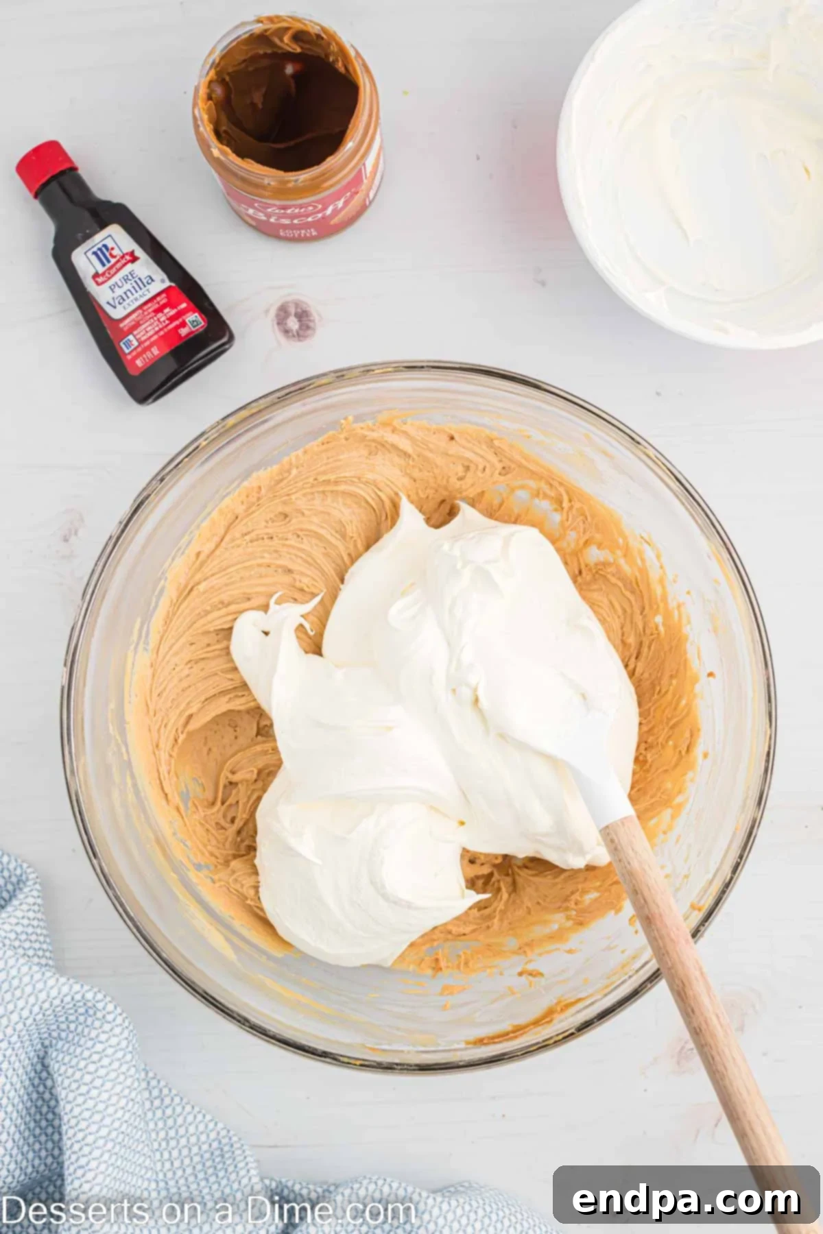 Decadent Cookie Butter Cheesecake 7 Whipped cream being gently folded into the smooth cookie butter cheesecake mixture in a mixing bowl.