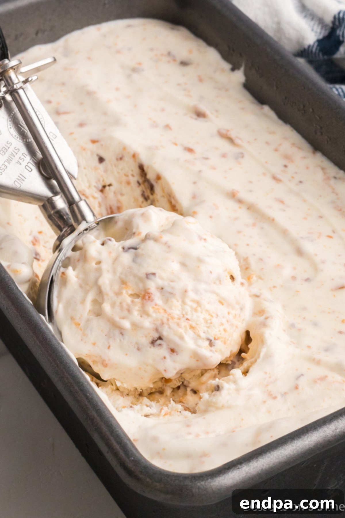 Homemade Butterfinger Crunch Ice Cream 10 A scoop of homemade Butterfinger ice cream being lifted from a loaf pan, showing its creamy texture and visible candy pieces.