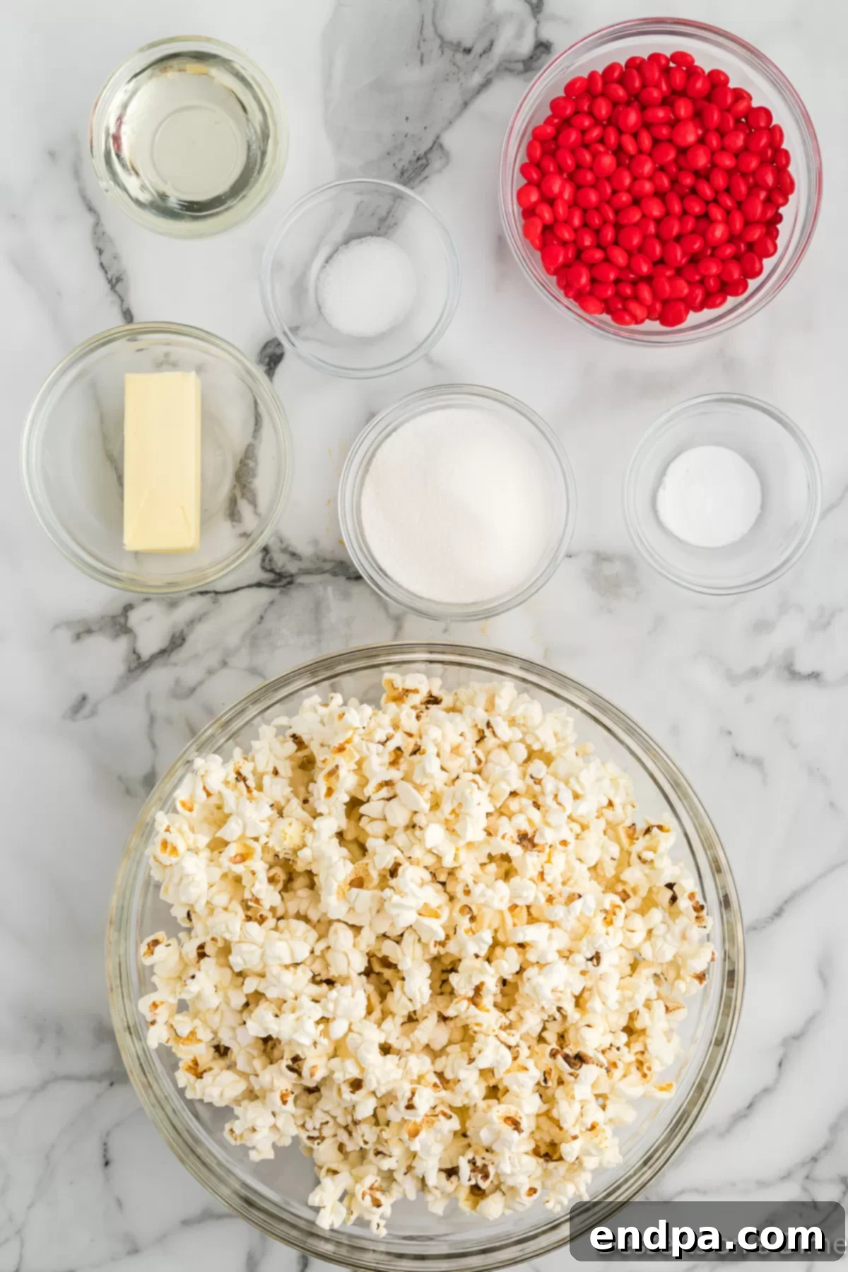 A flat lay showing the key ingredients for Red Hot Cinnamon Popcorn: popped popcorn, bright red hot candies, butter, and a small container of baking soda.