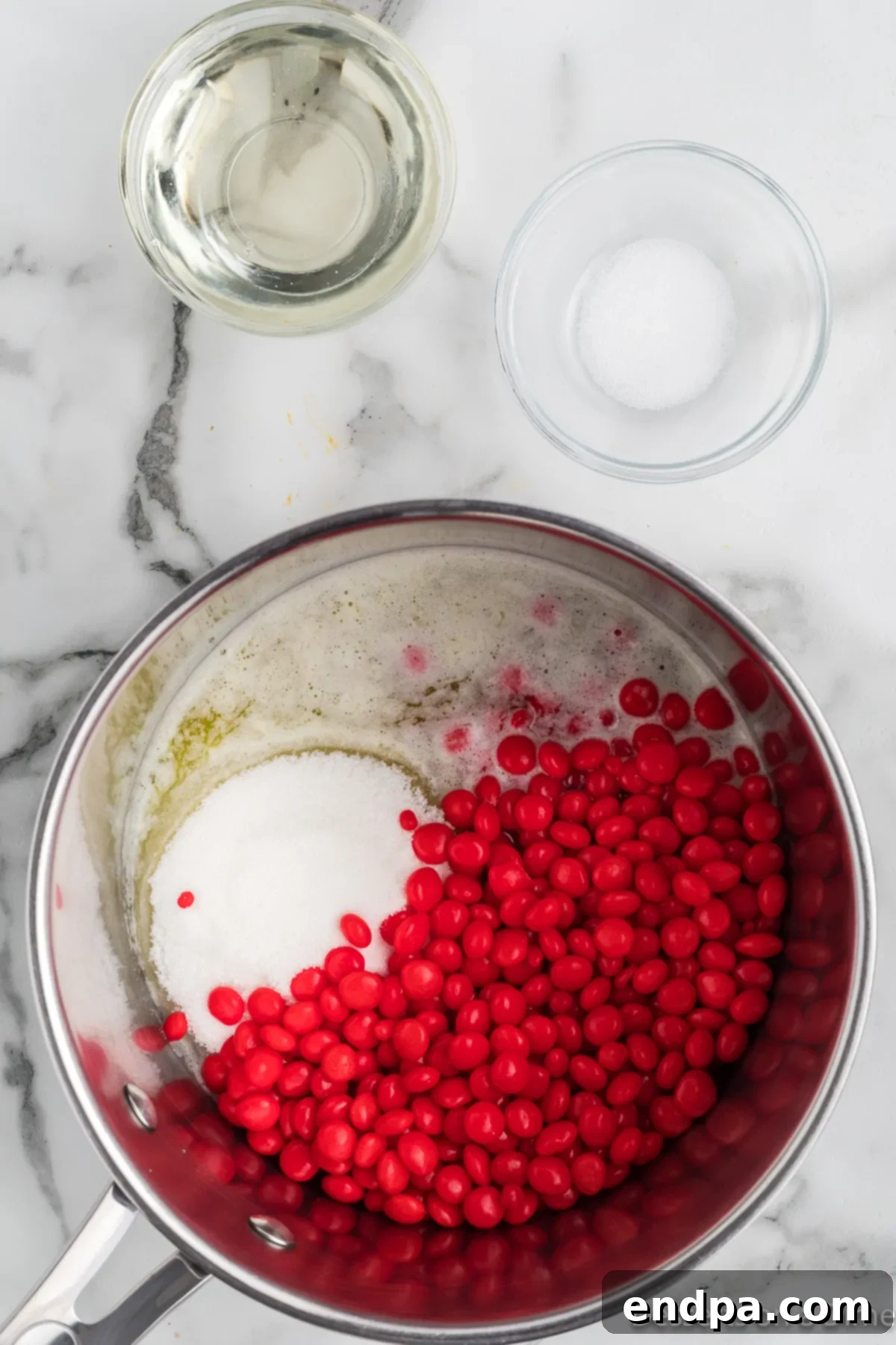 A saucepan on the stove with butter and red hot candies melting into a vibrant red liquid, ready for the next steps of the popcorn coating.