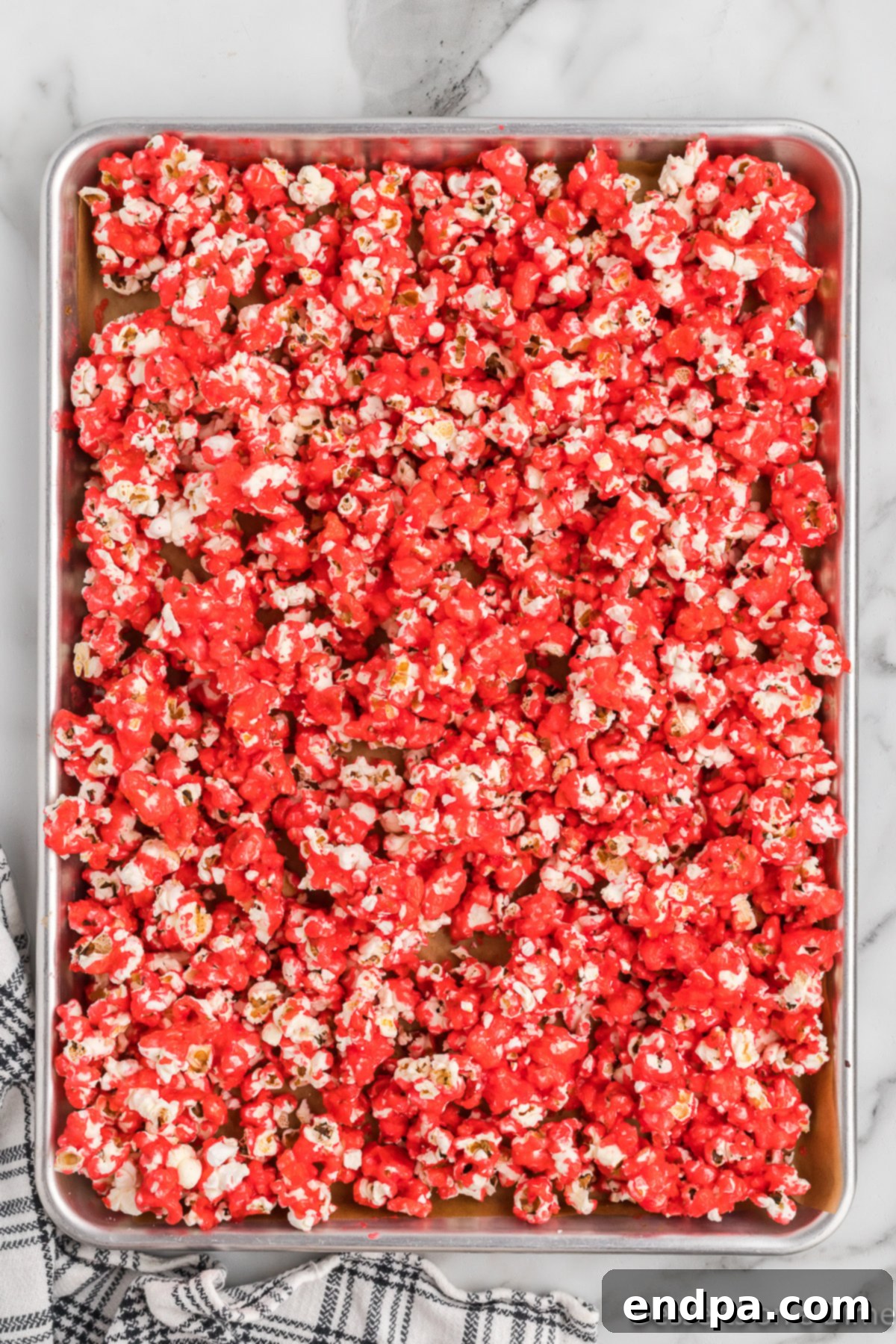 Red Hot Cinnamon Popcorn cooling on a baking sheet after being coated and baked, forming delicious, crispy clusters.