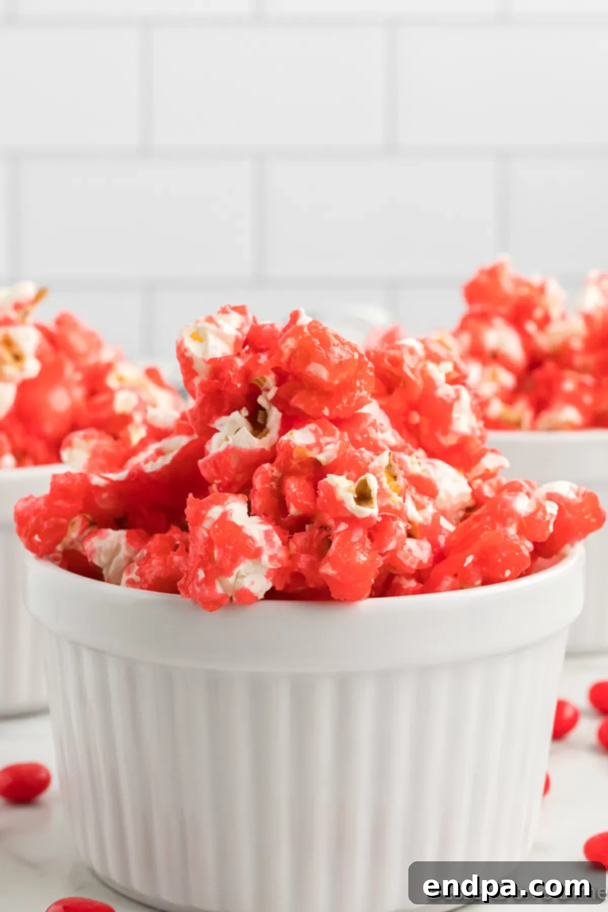A close-up shot of vibrant red hot cinnamon popcorn in a rustic ceramic bowl, showcasing its glossy candy coating and inviting texture.