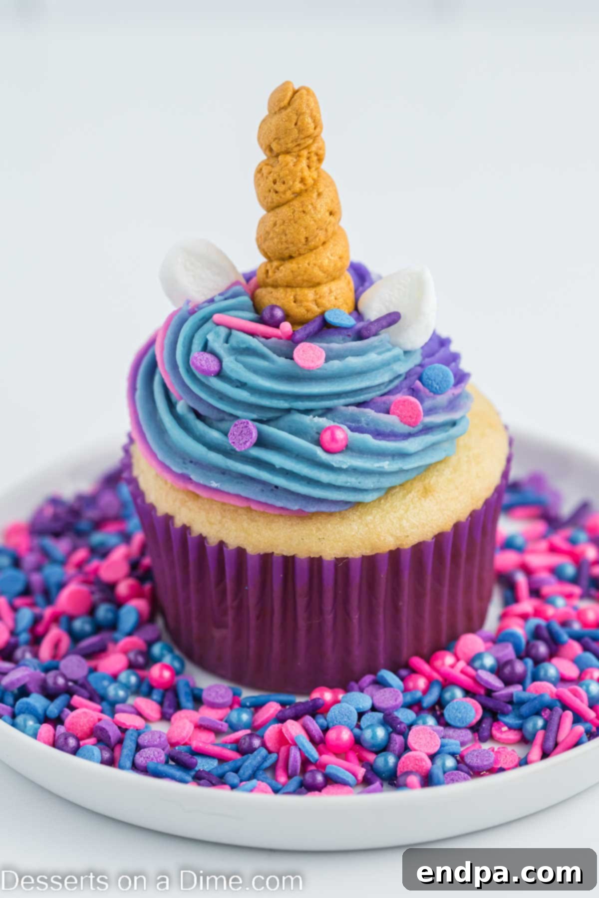 A single unicorn cupcake on a plate with scattered sprinkles.