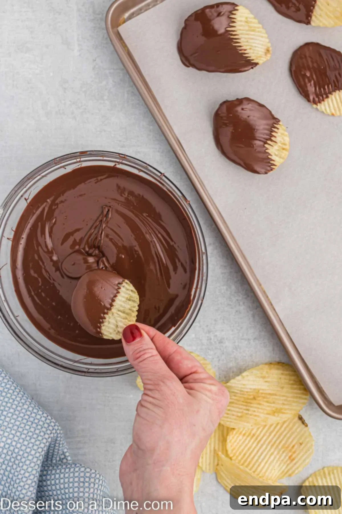 A chocolate-dipped potato chip being gently tapped on the bowl to remove excess chocolate.