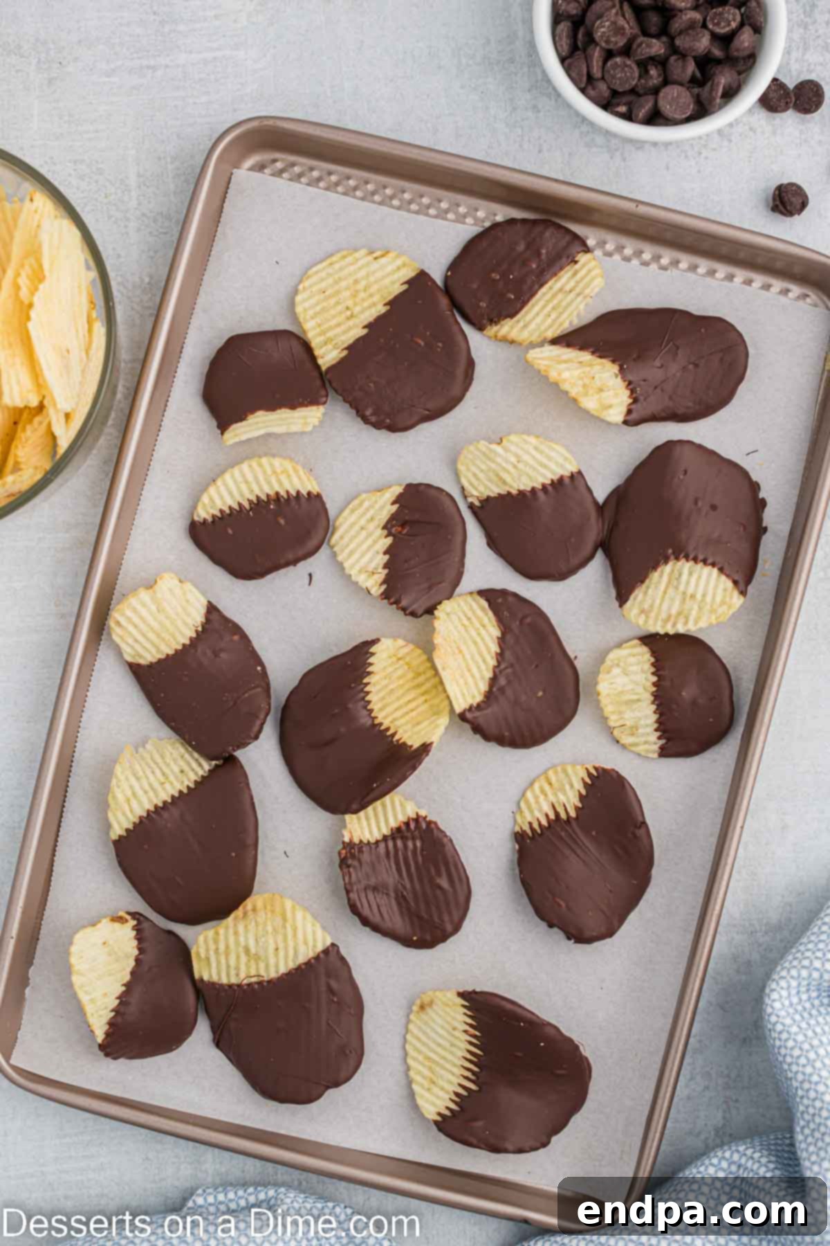 Chocolate-coated potato chips neatly arranged on a baking sheet, waiting to set.