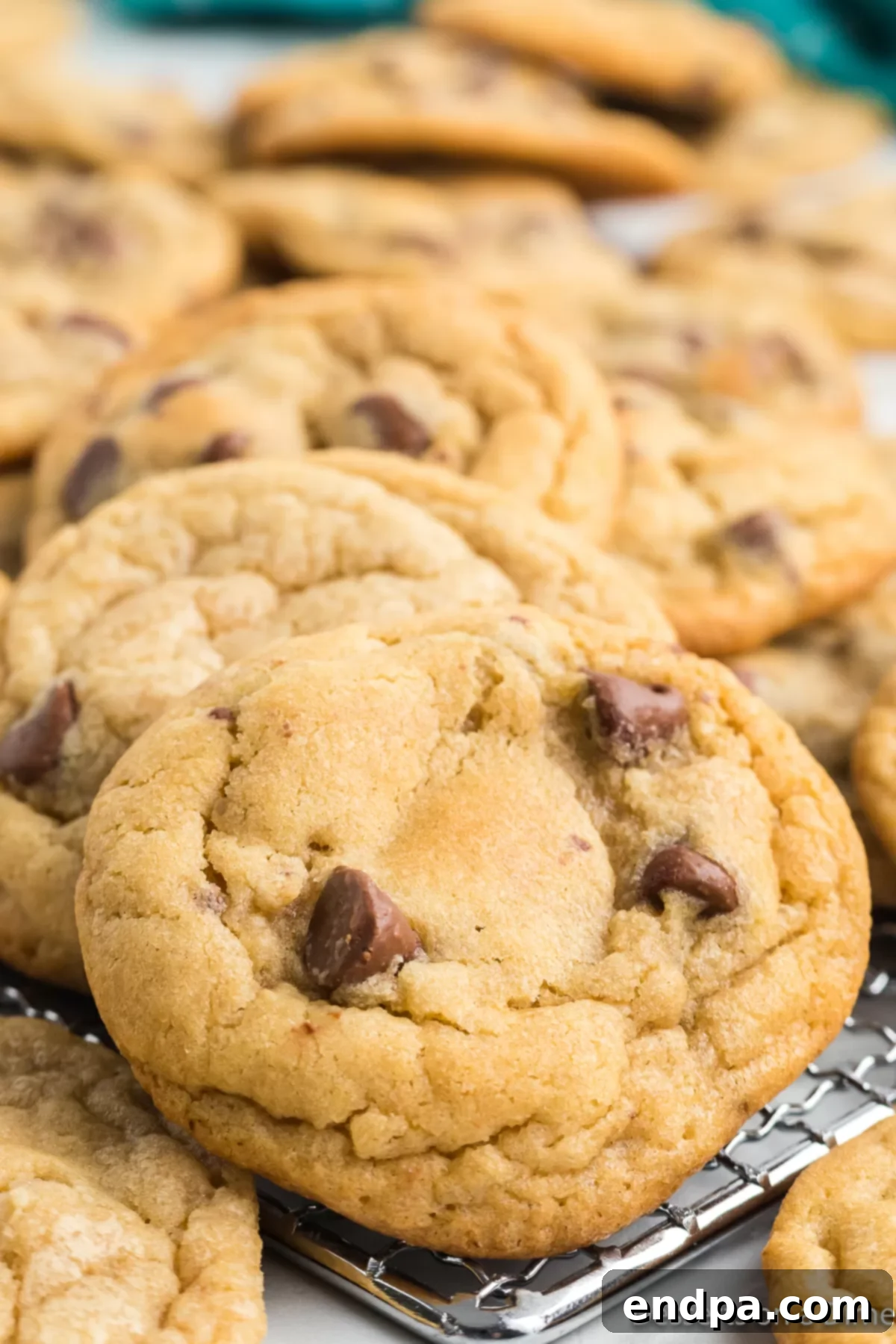Freshly baked Mrs. Fields-style chocolate chip cookies stacked on a cooling rack, glistening with melted chocolate.