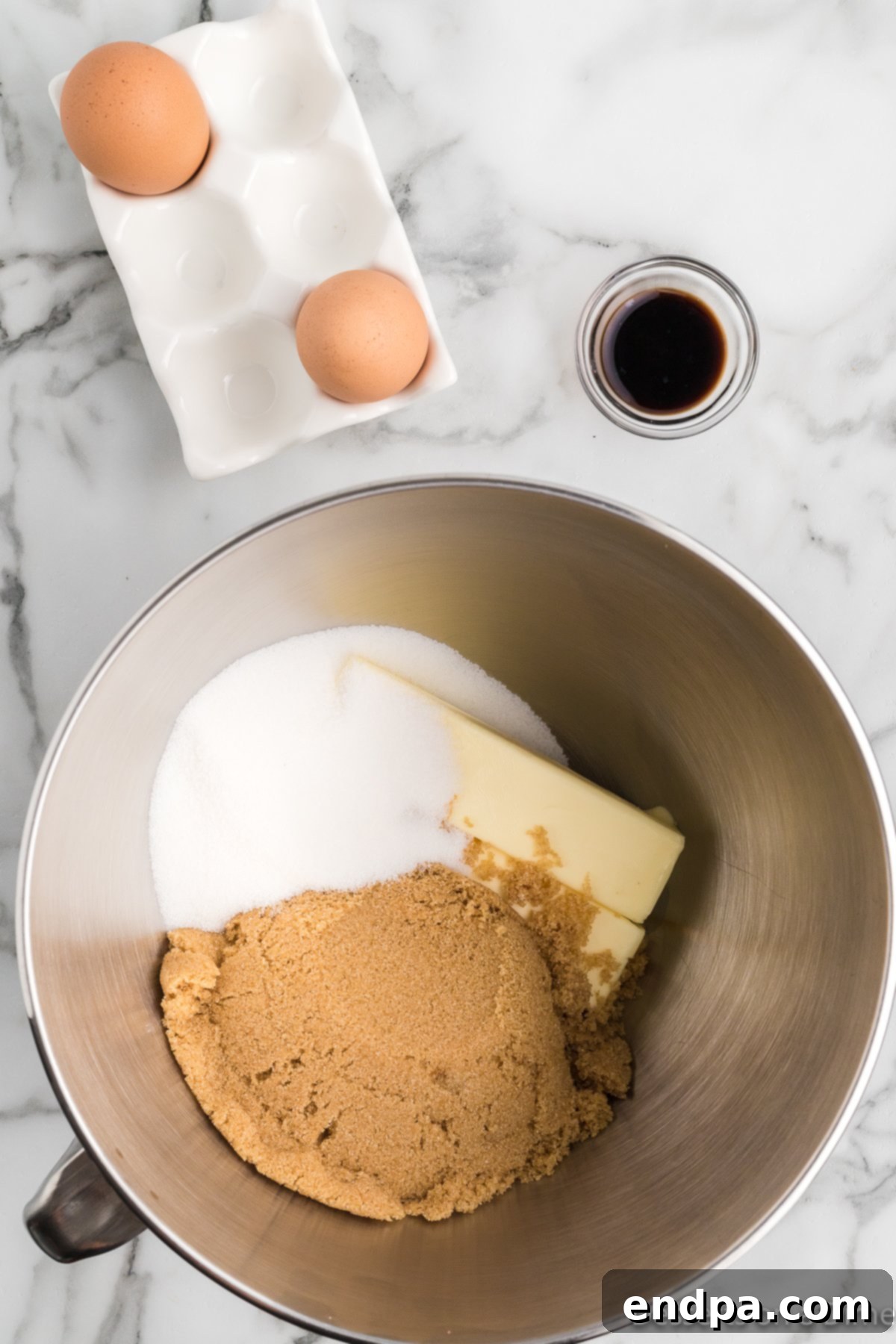 Mixing bowl with softened butter, granulated sugar, brown sugar, eggs, and vanilla extract combined together.