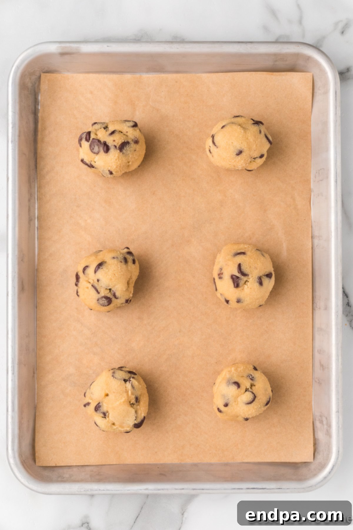 Cookie dough balls, about the size of golf balls, spaced on a parchment-lined baking sheet, ready for the oven.