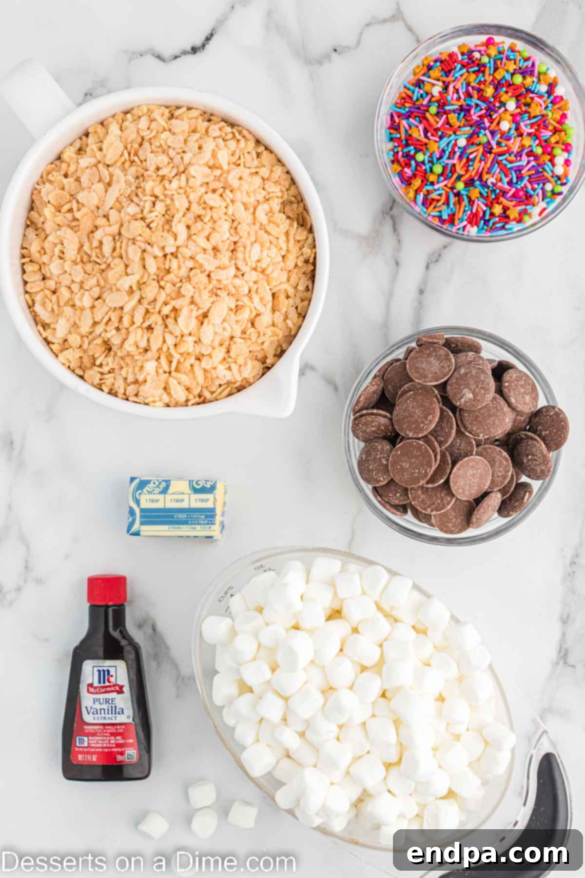 Ingredients for Chocolate dipped rice krispie treats laid out: rice krispie cereal, butter, mini marshmallows, vanilla, chocolate melting chips, sprinkles.