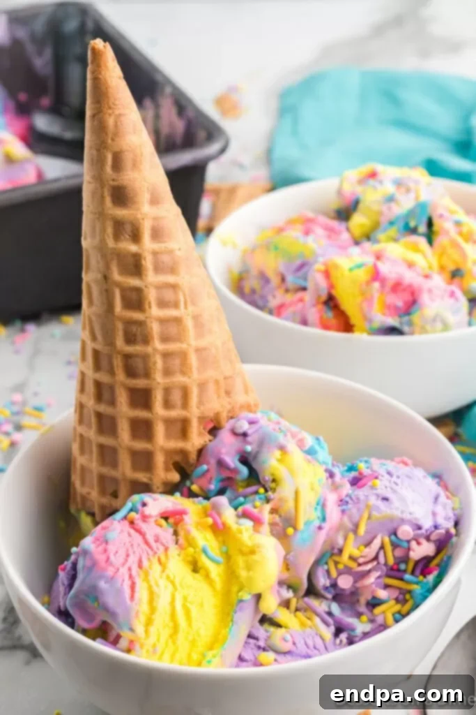 Rainbow Unicorn Dream 2 Unicorn Ice Cream in a bowl with a cone, showing off its vibrant rainbow layers and colorful sprinkles.