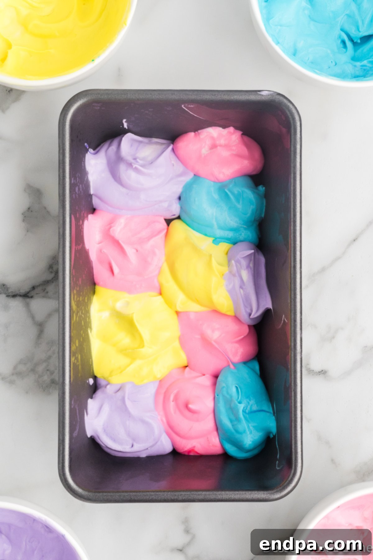 Rainbow Unicorn Dream 7 Ice cream mixture dolloped in colorful swirls into a loaf pan.