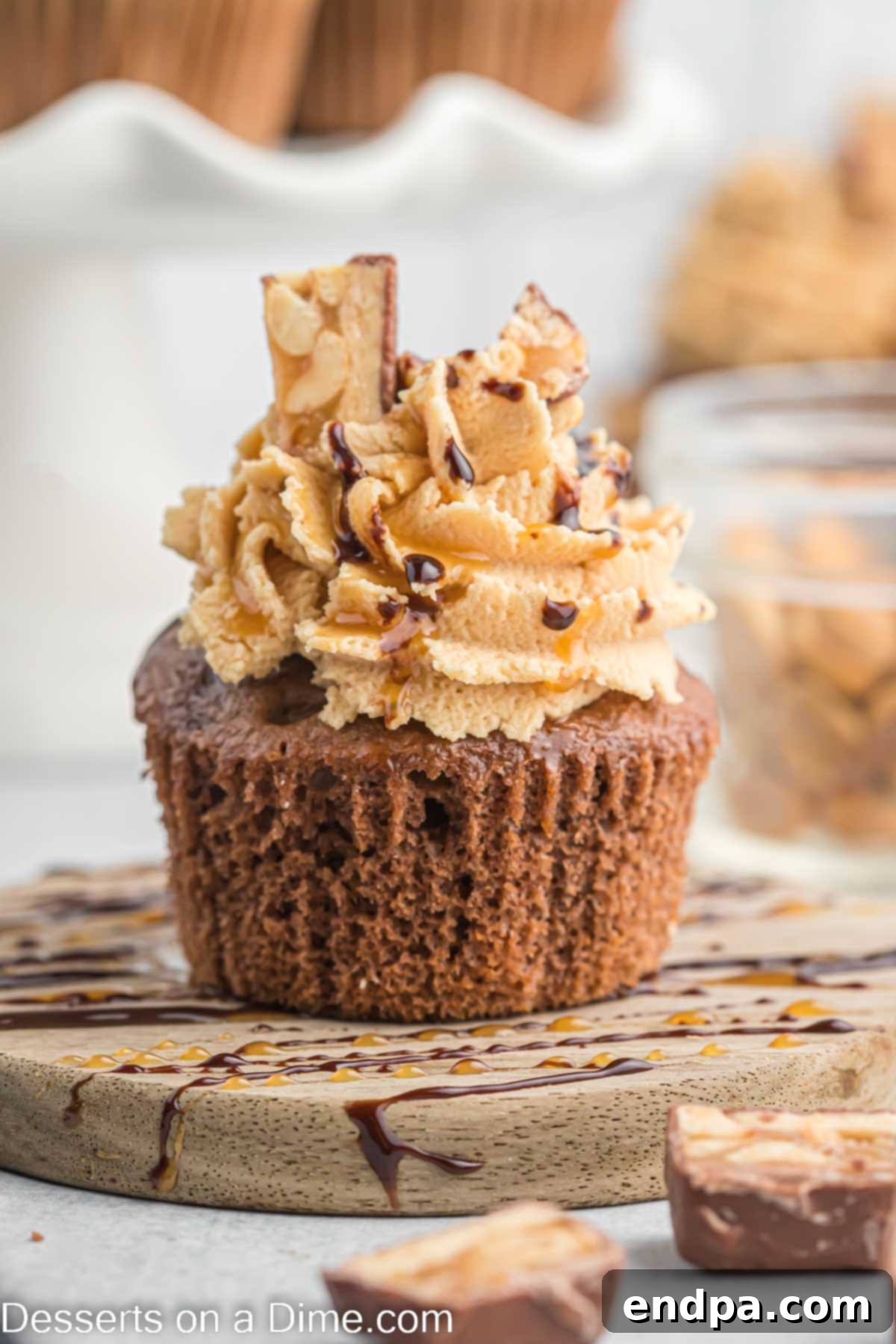A Snickers cupcake being drizzled with caramel and chocolate sauce, ready for final toppings.