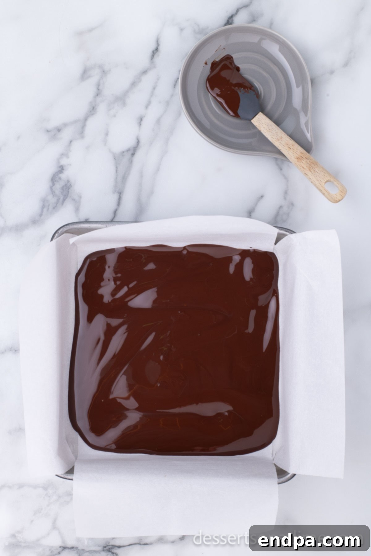 Easy Holiday Peppermint Bark 4 Melted dark chocolate spread evenly across the parchment-lined baking dish, forming the first layer.