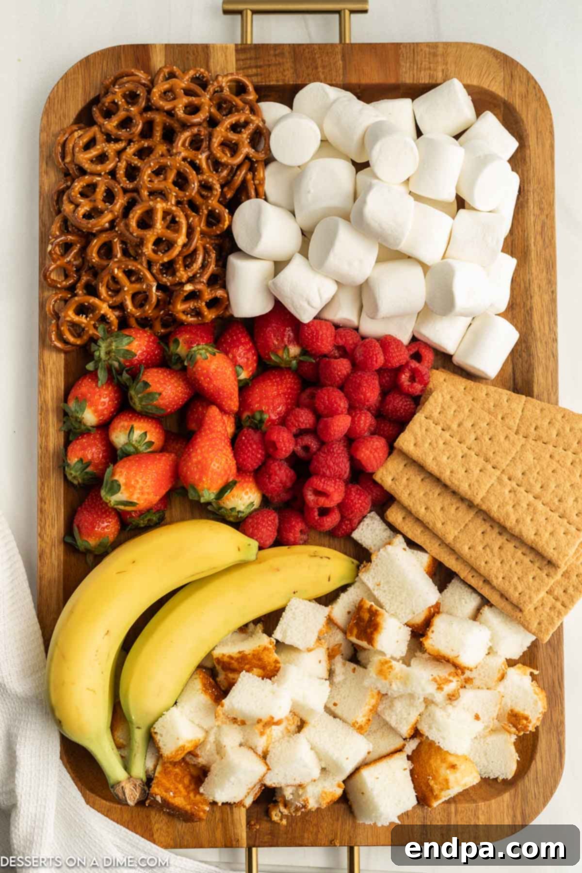 A beautifully arranged board with assorted dippers like fruit, cake, marshmallows, and pretzels, ready for chocolate fondue.