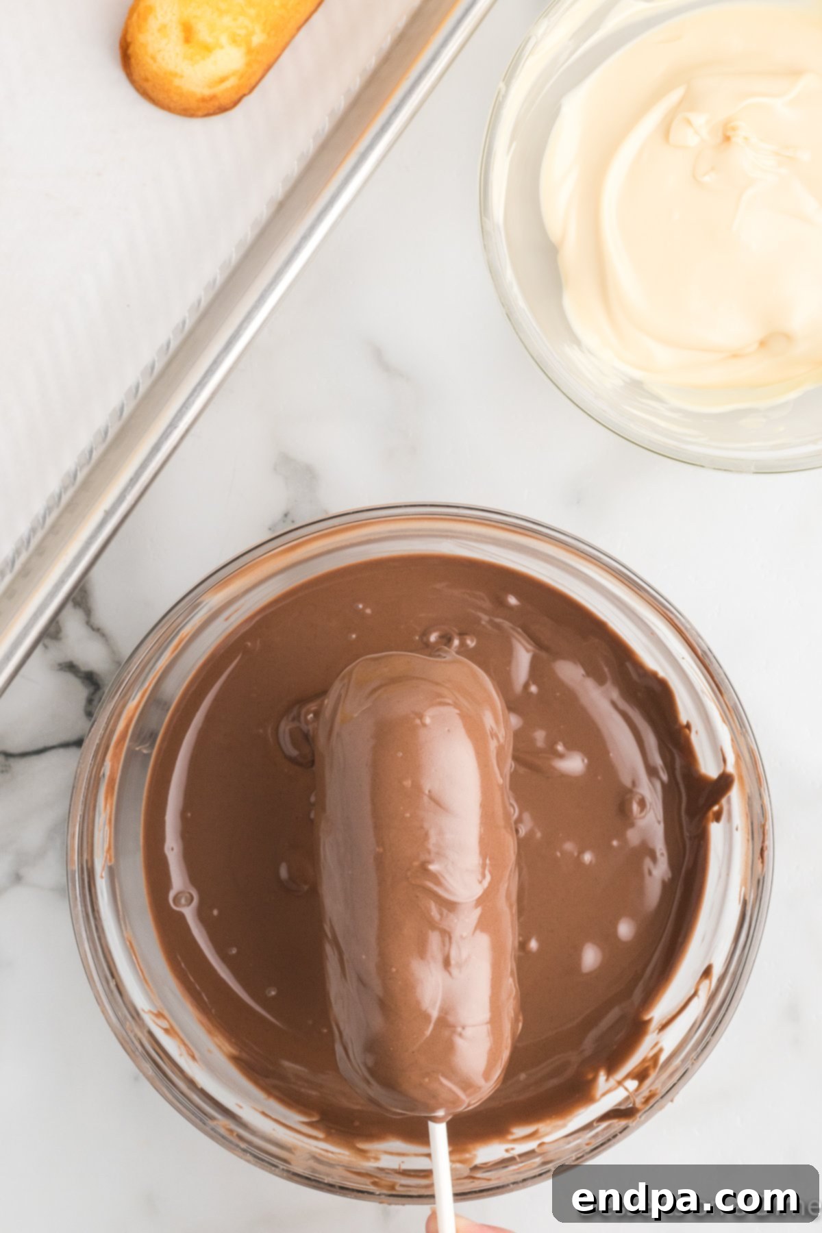 Decadent Chocolate Dipped Twinkies 6 A Twinkie being carefully dipped into a bowl of melted chocolate, ensuring full coverage.