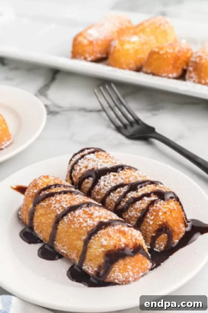 Crispy fried Twinkies on a plate, generously drizzled with rich chocolate syrup and a dusting of powdered sugar.