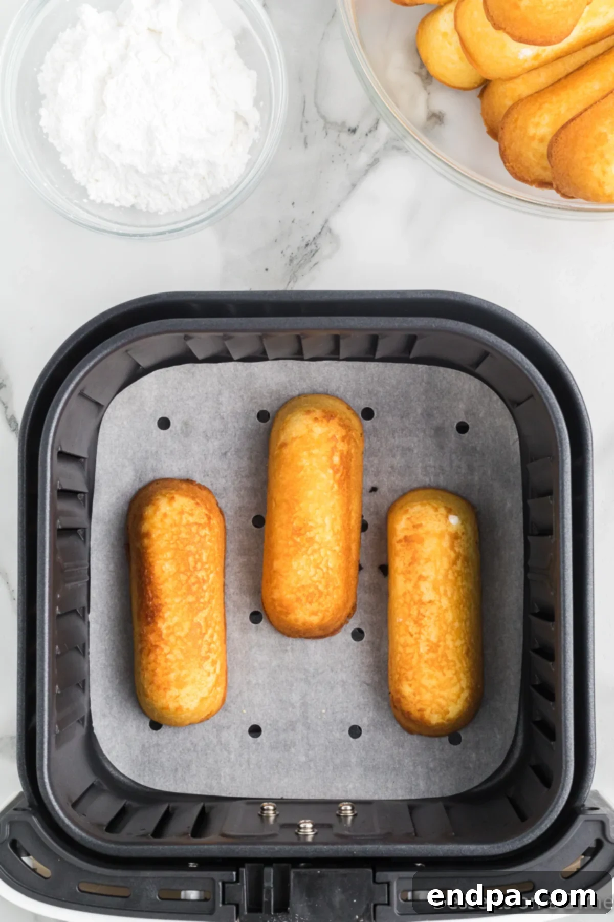 Twinkies in the air fryer basket after about one minute of cooking, showing a slight golden hue.