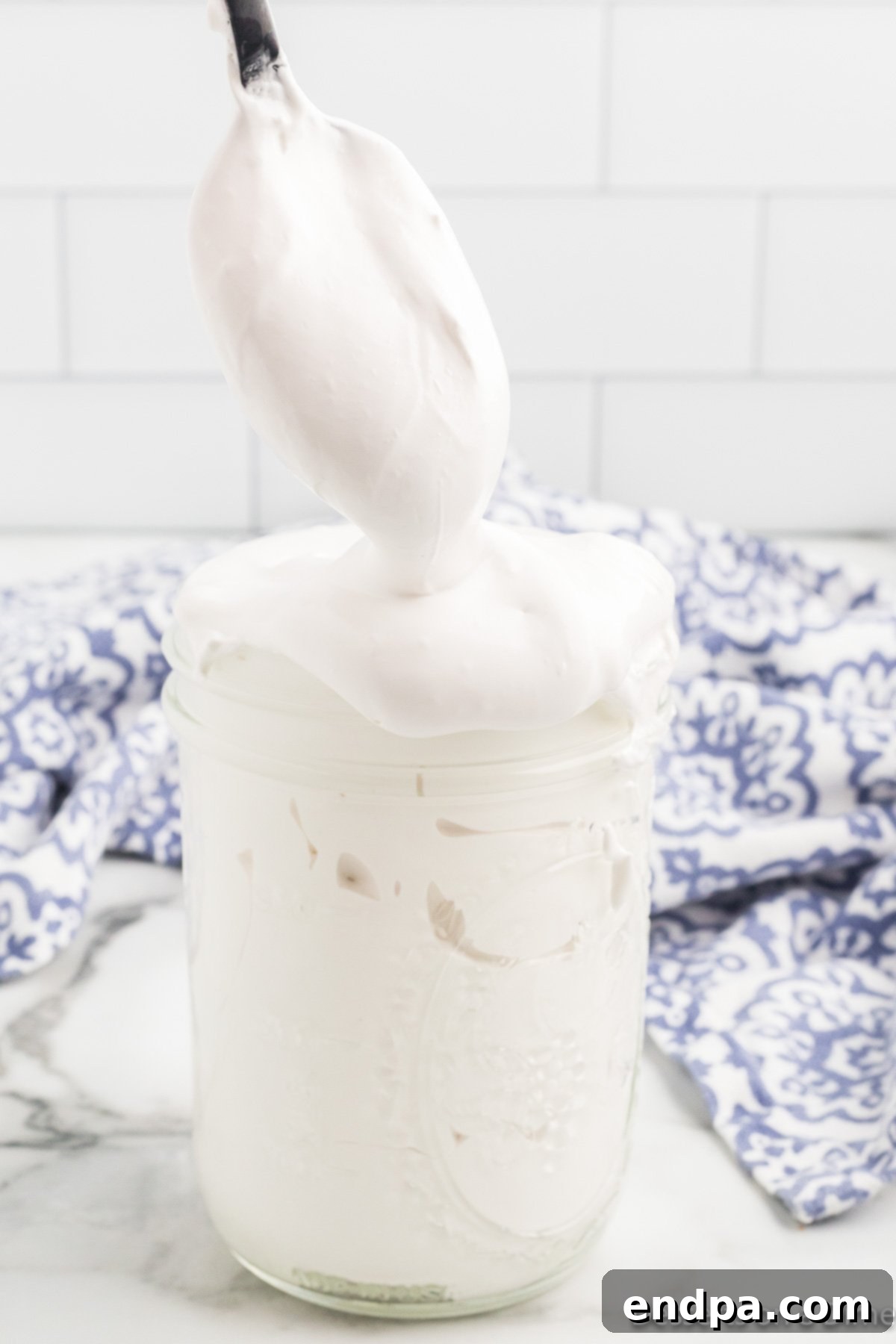 A spoon dipping into a jar of homemade marshmallow fluff, showing its thick and inviting texture.