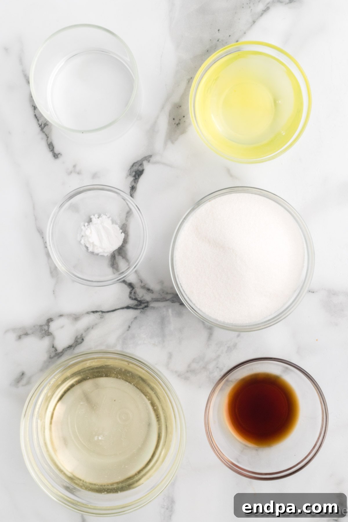 A spread of essential ingredients for homemade marshmallow fluff: granulated sugar, pure water, corn syrup, separated egg whites, a small bowl of cream of tartar, and fragrant vanilla extract.