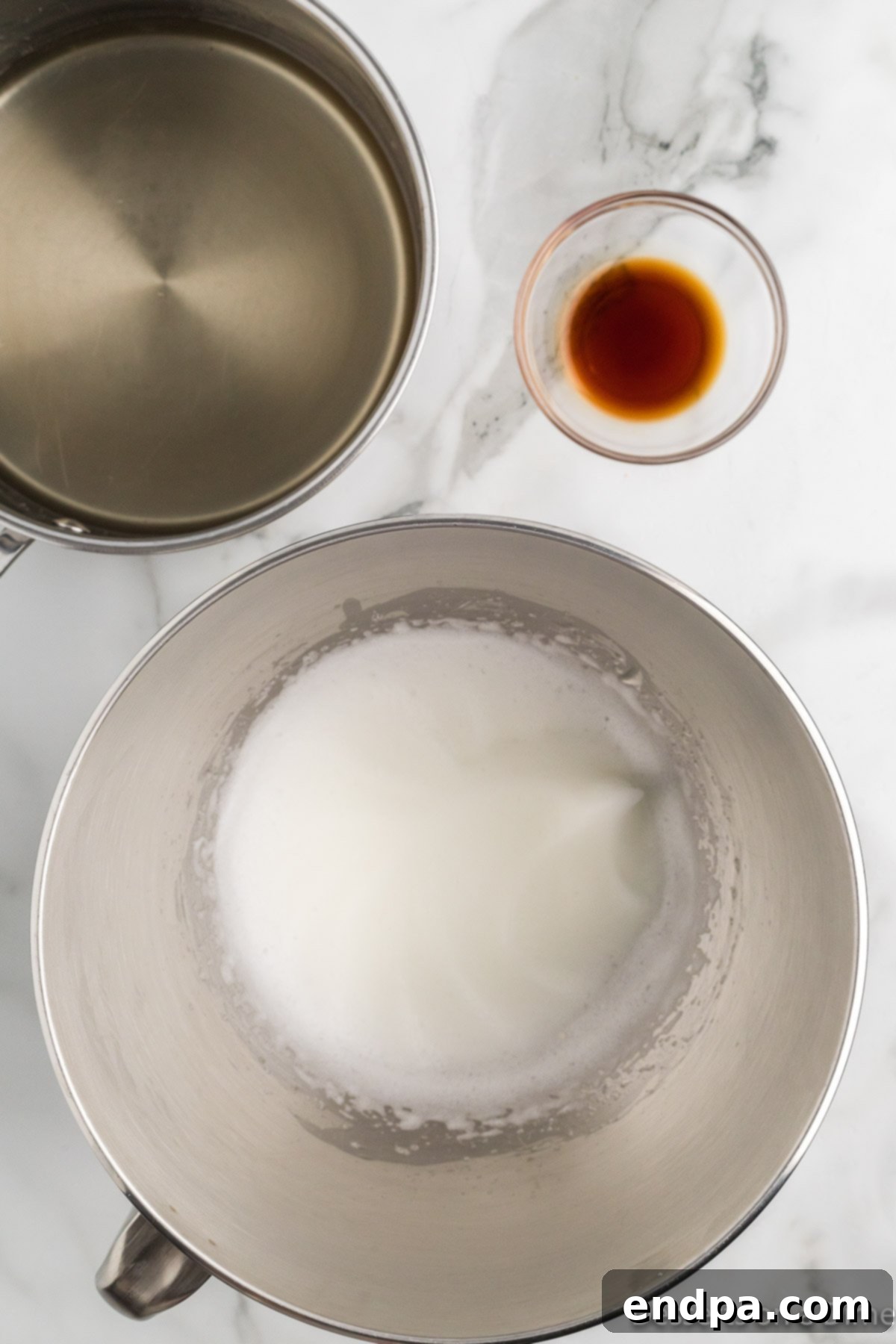 Egg whites and cream of tartar being beaten in a stand mixer with a whisk attachment.