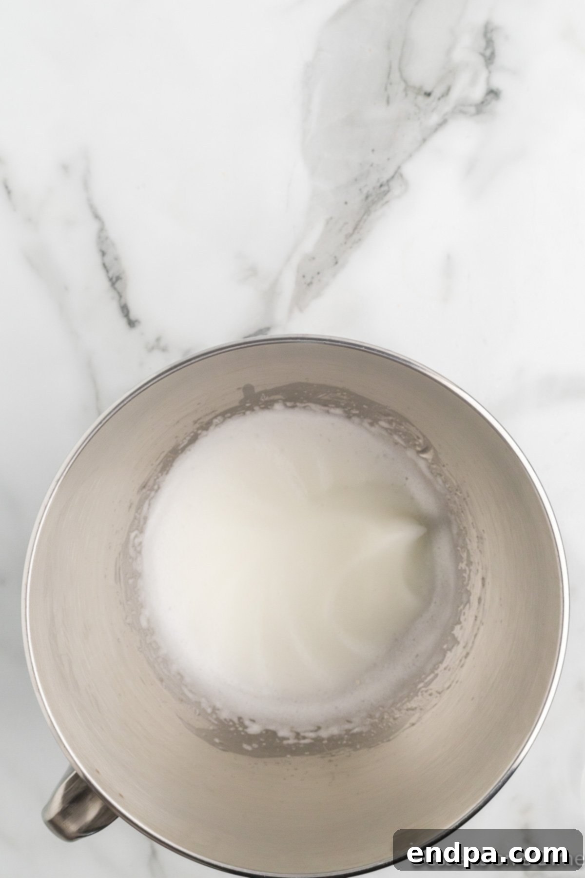 Stand mixer continuing to beat the egg white mixture, showing soft peaks forming.
