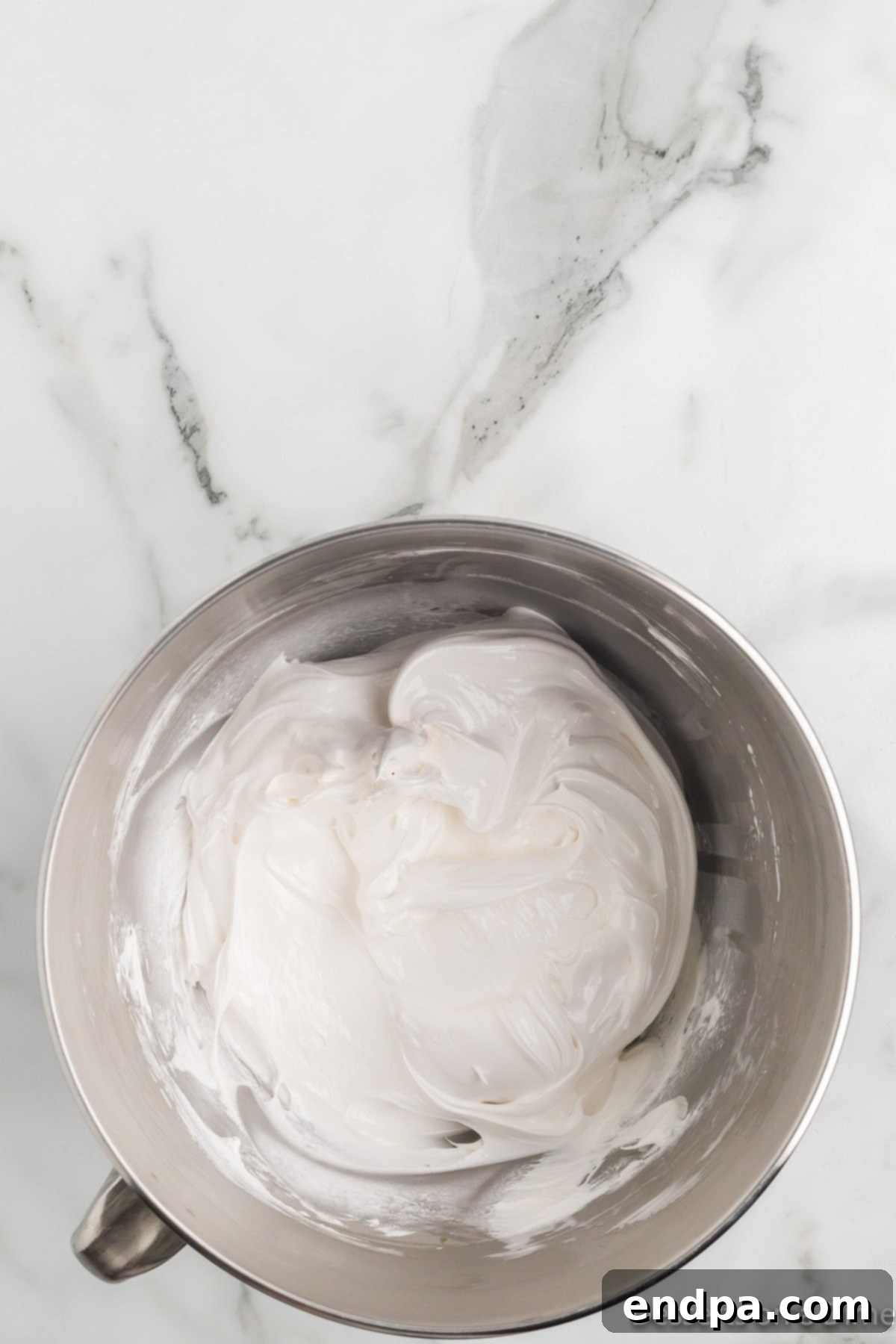 Hot sugar syrup being slowly drizzled into the whipped egg whites in a stand mixer on low speed.