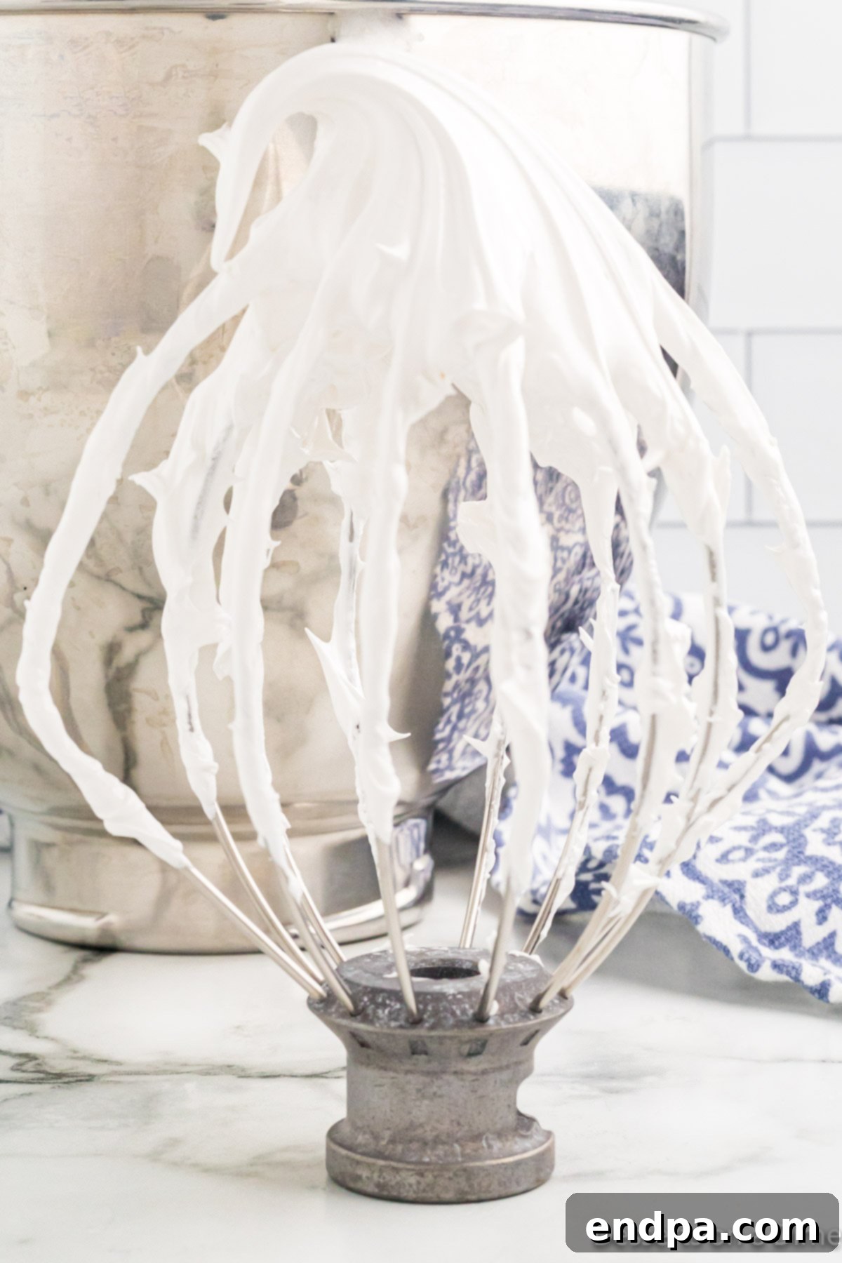 Stand mixer whisk attachment lifted, showcasing thick, glossy marshmallow cream clinging to it.