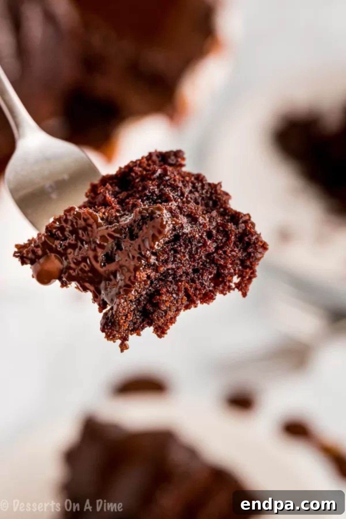 A fork holding a bite-sized piece of moist chocolate bundt cake with glaze.