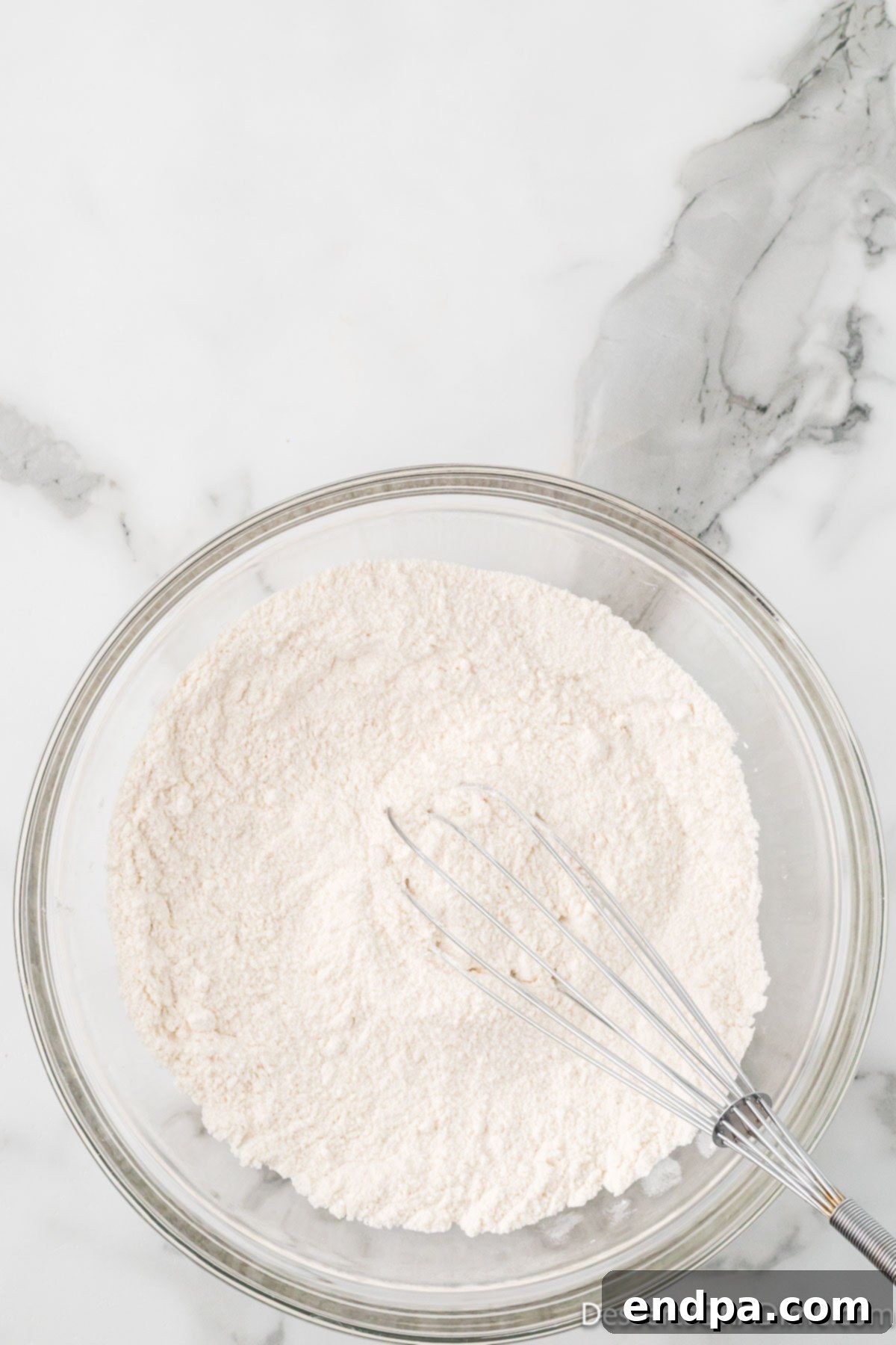 Mixing bowl with flour, granulated sugar, and baking soda being whisked together.