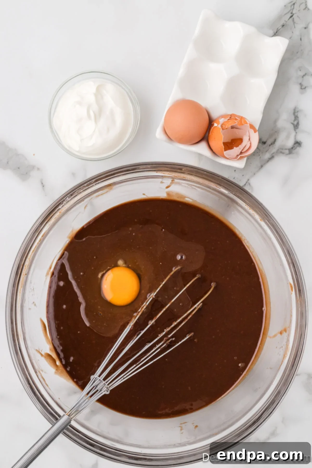 Eggs, sour cream, and vanilla extract being added to the cake batter in a mixing bowl.