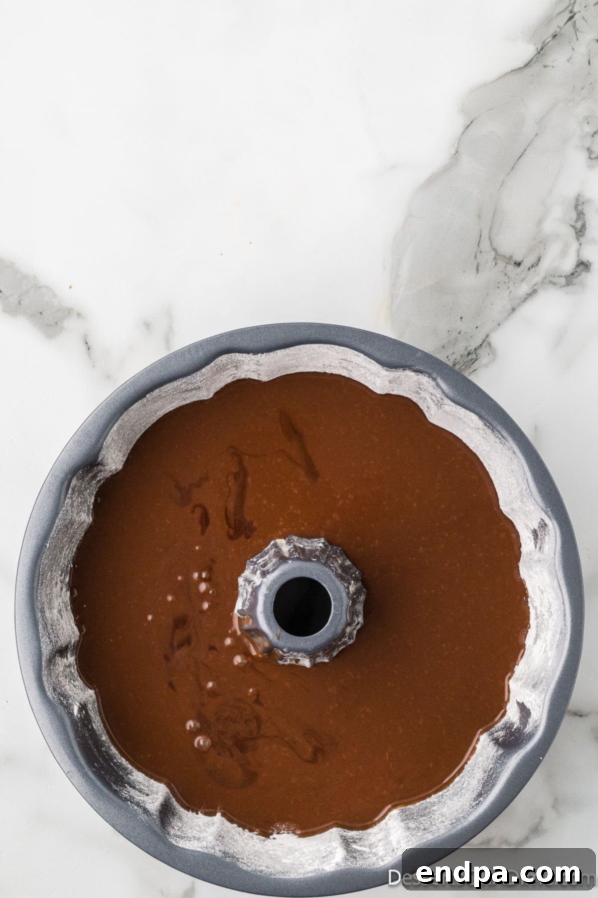 Chocolate bundt cake batter being carefully poured into a prepared bundt pan.