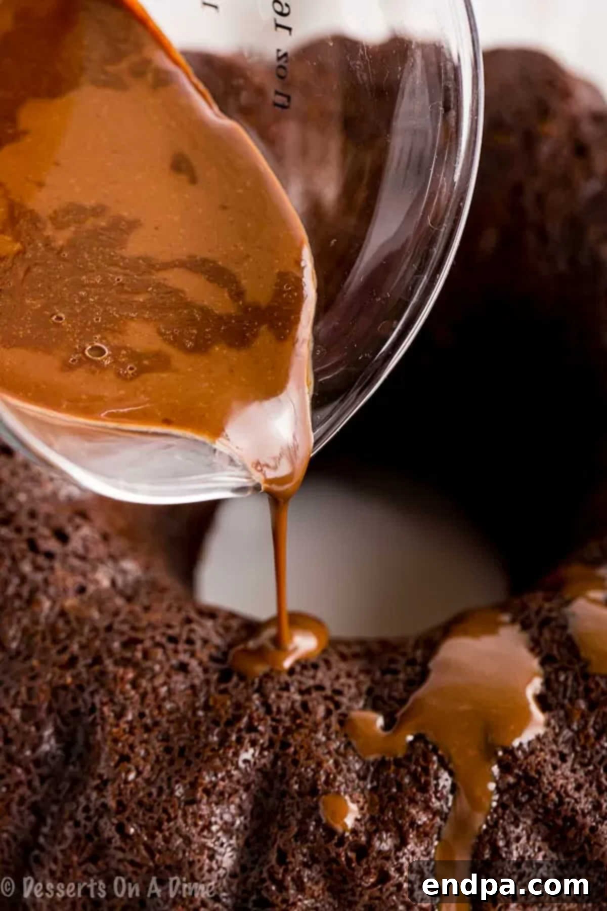 Smooth chocolate glaze being poured generously over a cooled chocolate bundt cake.