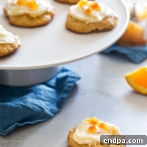 Soft orange cookies, elegantly frosted with cream cheese icing, arranged enticingly on a white plate.