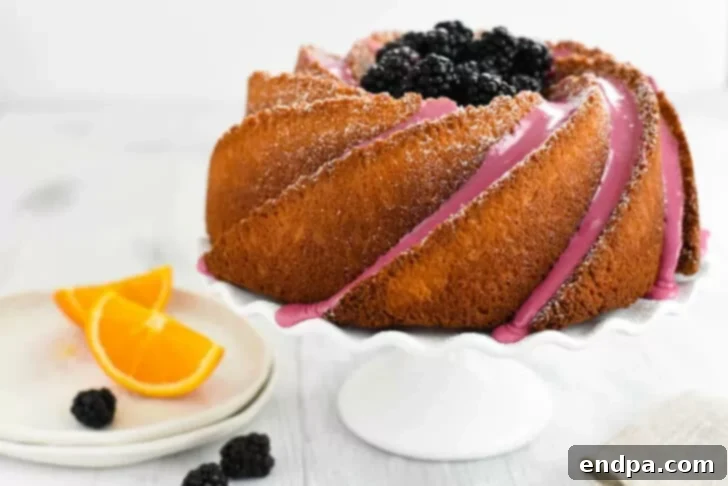 An exquisite orange bundt cake, generously drizzled with blackberry icing and garnished with fresh blackberries and orange slices.