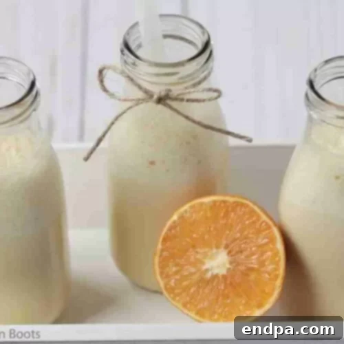 Three stylish bottles of creamy orange creamsicle milkshake, garnished with vibrant orange slices, ready for a refreshing sip.