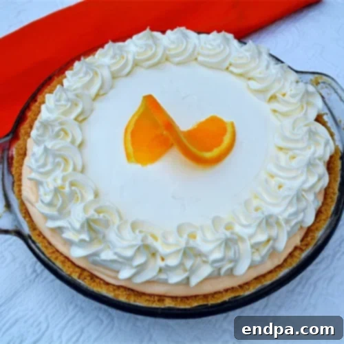 A delightful no-bake orange creamsicle pie, adorned with whipped cream and fresh orange slices.