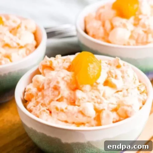 Three bowls of vibrant mandarin orange jello salad, garnished with fresh mandarin oranges, ready to be served.