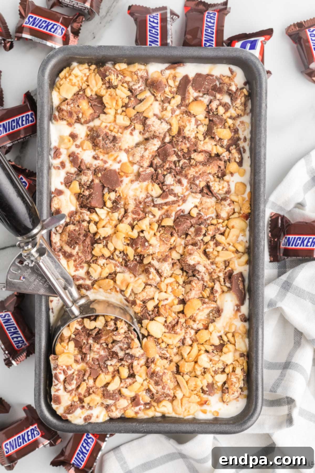 Decadent Homemade Snickers Ice Cream 11 A loaf pan filled with Snickers ice cream, topped with chopped candy and peanuts, covered in foil and ready for the freezer.